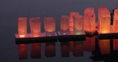 Bu anımsatıcı stok görüntüleri, alacakaranlıkta sakin suda sürüklenirken içeriden nazikçe aydınlatılan yüzen kağıt fenerlerin sakin sahnesini yakalar. Fenerler, yazıtlar ve tasarımlarla
