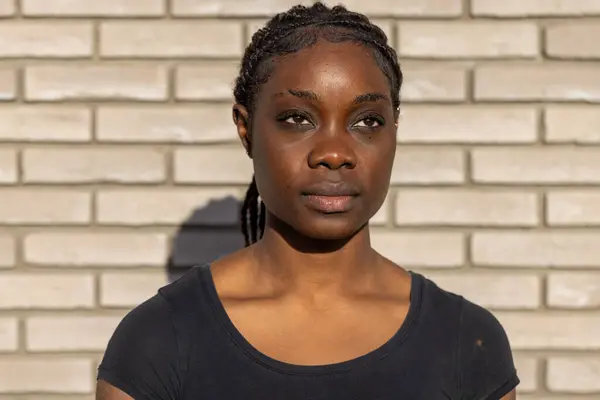 stock image This striking image captures a young African American woman with braided hair, exuding confidence as she looks directly into the camera. The sun casts a warm glow on her face, emphasizing her steady