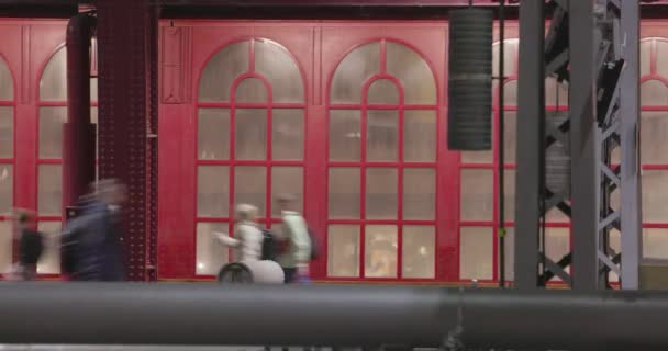 このストック映像は 独特の赤いドアを持つ歴史的な駅の背景に対して活動の混乱の中で移動する乗客のタイムラップを特徴としています 速いペースの動きはキャプチャします — ストック動画