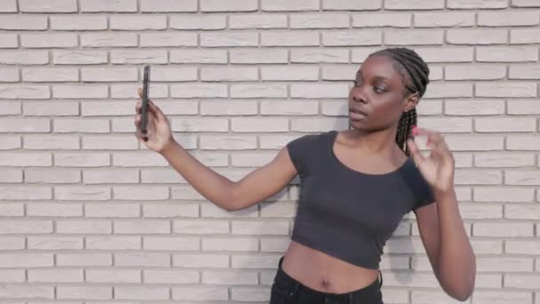 这个库存视频的特点是一个健康意识强的身穿运动服的年轻黑人妇女 检查她的健身应用智能手机与白色砖墙的对比 视频记录了一个时刻的准备或 — 图库视频影像