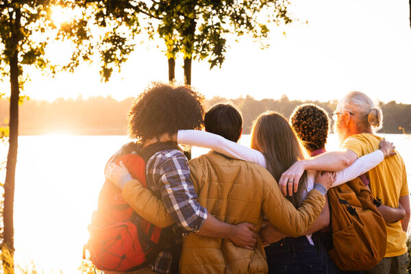 Этот образ пронизан теплотой заходящего солнца, когда он запечатлевает круг друзей, стоящих у озера, окутанный коллективными объятиями. Каждый человек частично смотрит в сторону от камеры