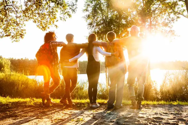 Backlit by the golden sun, a group of five friends shares an embrace, overlooking a peaceful lake. Friends Embracing the Sunset by a Serene Lakeside. High quality photo