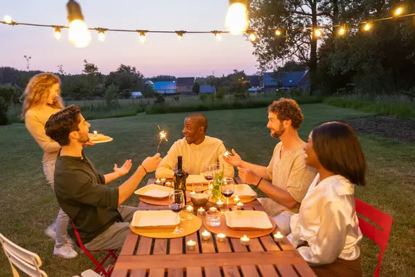 An intimate outdoor dinner party among friends, celebrating with sparklers under the gentle glow of string lights as dusk settles over the garden. Twilight Garden Party with Friends and Sparklers
