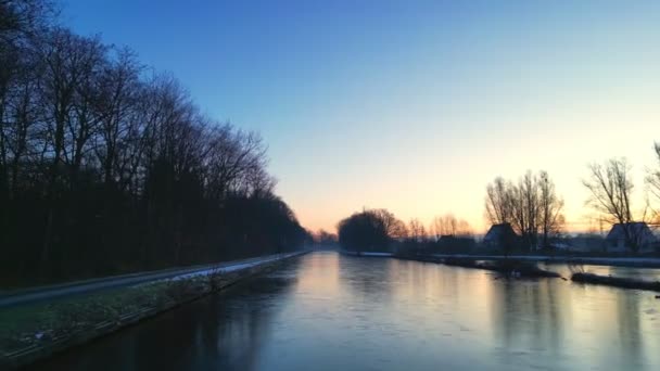 このストック映像は美しく鮮やかな冬の朝を撮影し 太陽は裸の木が並ぶ霜の多い運河の上に昇る 太陽の低い角度は氷の上に柔らかい黄金のライトを投げ 強調します — ストック動画