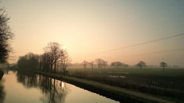 このストック映像は 穏やかな水路と眠った畑の上の早朝の霧の光の柔らかく拡散した光を捉えています 昇る太陽は穏やかな光を投げ 木のシルエットと平和を創造する — ストック動画