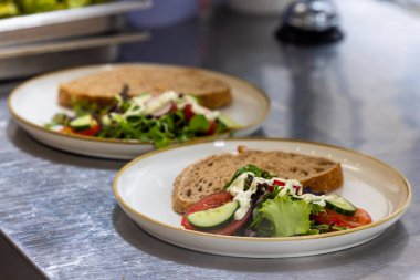 Bu resim, her birine bir dilim tam tahıllı ekmek eşlik eden bir restoran ortamında yeni hazırlanmış iki tabak salatayı gösteriyor. Salatalar iyi hazırlanmış, yeşillik çeşitleri var.