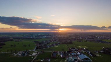 Kırsal bir arazinin havadan çekilmiş bu fotoğrafında güneş ufkun altına batıyor, çiftlikler ve çiftlikler üzerine sıcak bir ışıltı saçıyor. Geniş bulut manzarası huzur sahnesine dram katıyor.