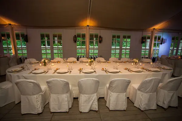stock image A sophisticated banquet hall, ready for guests, with tables dressed in pristine white linens and adorned with delicate floral arrangements. The intimate lighting casts a warm glow, complementing the