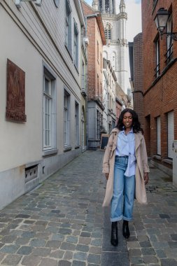 Bu görüntüde, genç siyah bir kadın Avrupa 'nın tuhaf bir yan sokağı boyunca sakin bir şekilde geziniyor. Çağdaş kıyafetinin içinde tarz ve konfor yayıyor. Açık mavi bir gömlek, şık bir şekilde.
