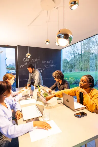 A dynamic team meeting in a well-lit modern workspace. The photograph captures a group of focused professionals, of diverse backgrounds, brainstorming around a sleek conference table, with a