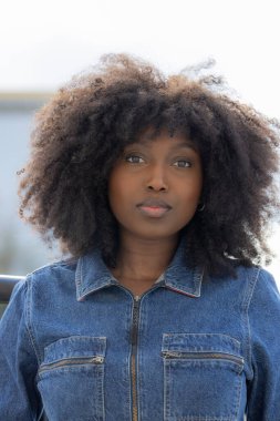 This portrait exudes serenity, featuring a woman with a full, natural afro hairstyle. The denim jacket she wears adds a timeless quality to her look. Her gentle gaze and soft expression suggest an clipart