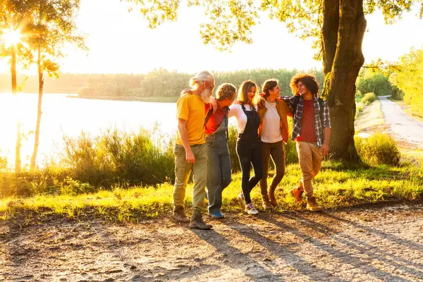Five friends walking along a lakeside path, bathed in the warm glow of sunset. Group of Friends Enjoying Sunset Walk by the Lake. High quality photo