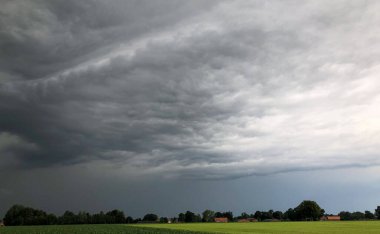Görüntü, derin derin düşünen fırtına bulutları ile aşağıdaki sakin kırsal kesim arasındaki dramatik zıtlığı net bir şekilde yakalıyor. Yaklaşan bulutlar yaklaşan bir fırtınayı işaret ediyor, dinamik ve...