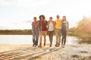 Güneş batarken deniz kenarında beş gezintiden oluşan bir grup gündelik gezintilerine hafif bir ışık saçıyor. Dusk 'taki Lakeshore boyunca birbirine bağlı arkadaşlar birlikte yürüyor. Yüksek kalite fotoğraf
