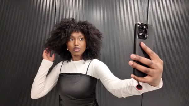 一連の画像は エレベーターでセルフィーを取る活発で表現的なアフリカ系アメリカ人の黒人女性を描いています 彼女は自信を持って彼女のスマートフォンとポーズし 異なる角度で実験します — ストック動画