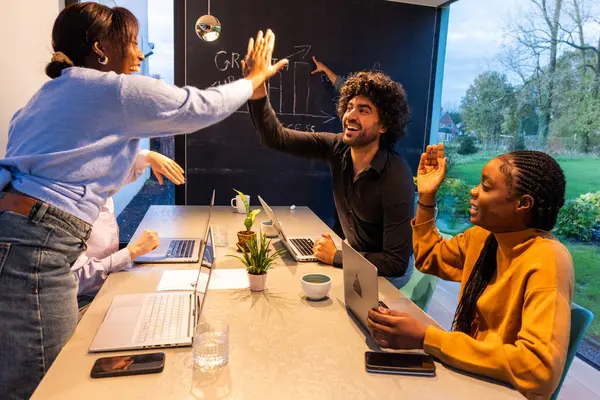 Modern bir ofiste, Asyalı bir kadın, Orta Doğulu bir erkek ve siyahi bir kadının yer aldığı coşkulu bir an. Laptoplarla dolu parlak, mermer bir masanın etrafında toplanırlar.