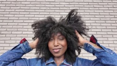 Şık genç bir kadının şehvetli afro saçlarını şaklabanca ayarlarken, çarpıcı bir şehir tuğlası duvara yaslanırken, modern ve tasasız ruhunu ön plana çıkarırken, büyüleyici yavaş çekim görüntüleri. Şık Genç