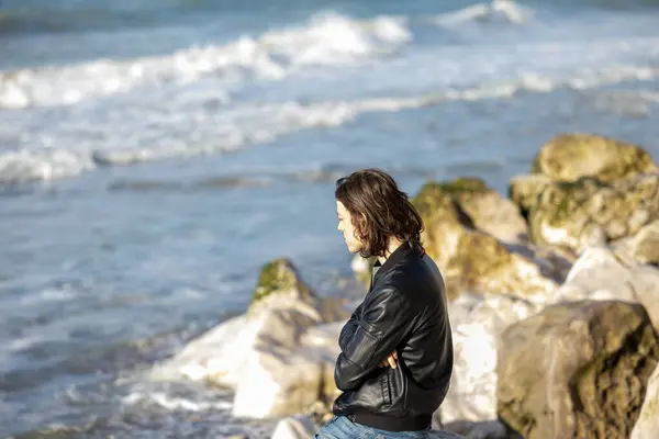 A contemplative woman gazes out at the sea from a rocky beach, Lost in deep thought and serene solitude