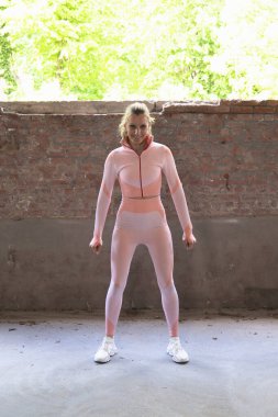 Tuğla duvarın önünde gülümseyen pembe spor kıyafetli bir kadın egzersiz ve sağlıklı yaşam tarzına kendini adamış.