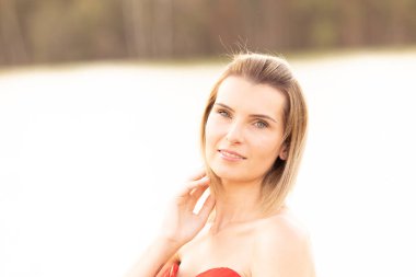 Sade bir açık hava portresi, güneş ışığı altında, yumuşak, doğal bir arka plan karşısında kırmızı elbiseli bir kadını yakalar.