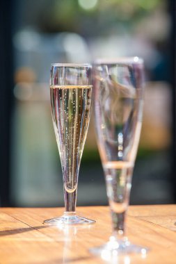 İki zarif şampanya kadehi açık havada güneş ışığında bir masanın üzerinde şenlikli ve lüks bir atmosfer yaratıyor.
