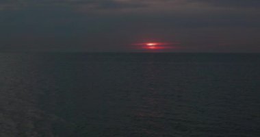 Huzurlu bir denizin üzerinde sersemletici bir gün batımı, kararmış bir gökyüzüne vuran canlı kırmızı güneş. Huzurlu ve huzurlu.