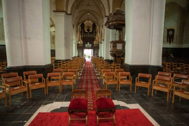 Ahşap sandalyeler, kırmızı halı ve dekoratif mimari içeren tarihi bir kilisenin simetrik manzarası..