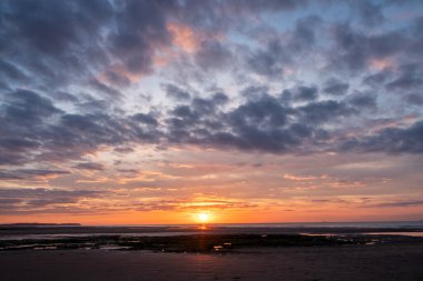 Canlı renklerle büyüleyici bir gün batımı, sakin bir sahil ve sakin bir okyanus, sakin ve huzurlu bir atmosfer yaratıyor.