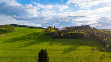 Bereketli yeşil tarlaların, yuvarlanan tepelerin manzarası ve bulutlarla dolu canlı bir gökyüzü muhteşem bir manzara yaratır.