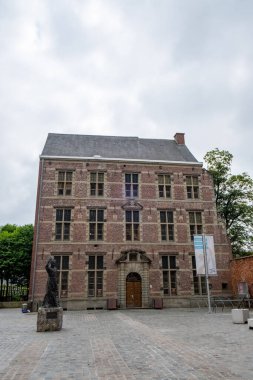 Halle, Belçika, 15 Mayıs 2024, önünde gökyüzüne karşı dikilen heykeli olan büyük tuğla bir bina. Mimari, şehir yapısına klasik bir yapı kazandıran karmaşık tuğla işçiliğine sahip.