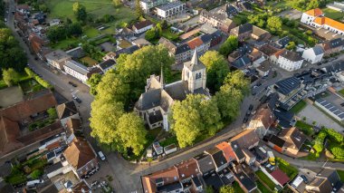 Sint-Pieters-Leeuw, Brüksel, Belçika, 4 Haziran 2024. Huzurlu bir kasabadaki yemyeşil ağaçlarla çevrili tarihi bir kilise manzarası..