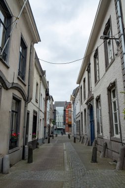 Halle, Belçika, 15 Mayıs 2024, bulutlu bir günde iki bina arasında dar bir ara sokak, pencereleri, cepheleri ve bileşik malzeme altyapısını gösteriyor. Yol yüzeyi de görülebilir.