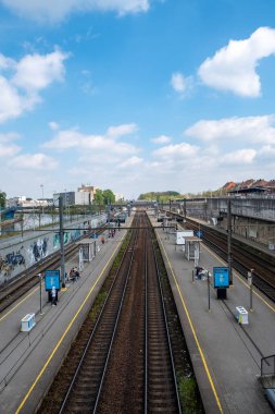 Halle, Belçika, 15 Mayıs, 2024, Sahne bulutların, binaların, araçların ve ulaşım altyapılarının gösterildiği güneşli bir günde yukarıdan açık bir gökyüzünün altındaki tren istasyonunu tasvir ediyor.