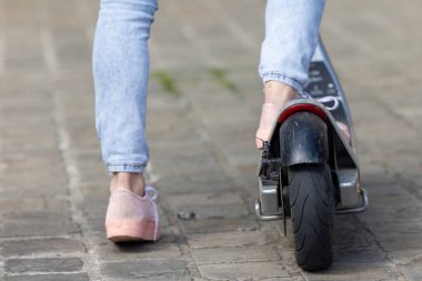Rahat ayakkabılar giyerken, düz bir yüzeyde elektrikli scooter kullanan birinin bacaklarının yakın plan görüntüsü.