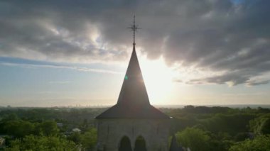 Günbatımına karşı koyan, etrafında yeşil manzaralı, silüet bir kilise kulesinin dramatik bir sahnesi var.
