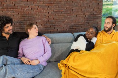 Bir grup arkadaş birlikte vakit geçiriyorlar, kanepede battaniyelerle dinleniyorlar, samimi ve neşeli bir ortam..