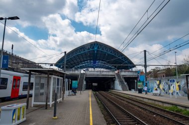 Halle, Belçika, 15 Mayıs, 2024, Bir tren istasyonu arkasında bir tren olan mavi bir çatıya sahiptir, bulutlar, gökyüzü, bina, araç, ray gibi elementler ve bir tren yolu üzerinde bir ulaşım modu ima eder.