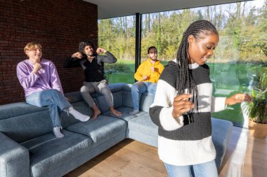 A group of friends is enjoying themselves, dancing and having fun in a modern living room with a beautiful outdoor view clipart