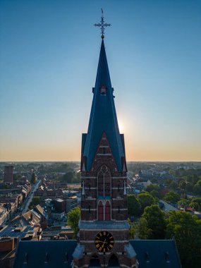 Gökyüzünden çekilen, büyüleyici gündoğumu arkaplanı altında antik bir kilise kulesinin çarpıcı görüntüsü.