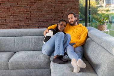 Bir çift rahat bir oturma odasında kanepede dinleniyor, birbirlerine eşlik ederek ve rahat bir ortamda eğleniyorlar.