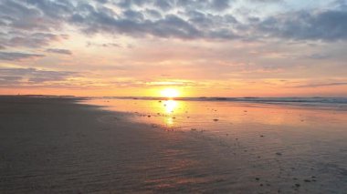 Huzurlu bir plajda baş döndürücü bir gün doğumu, sabahın erken saatlerinde kumlara yansıyan ışığın güzelliğini gözler önüne seriyor. Gökyüzü turuncu ve pembe yumuşak renklerle boyanırken, yumuşak dalgalar üzerinde yuvarlanıyor.