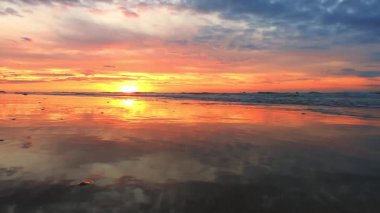 Güzel kumsalda, sersemletici bir günbatımı ıslak kumları, dalgaları ve renkli gökyüzünü aydınlatır.