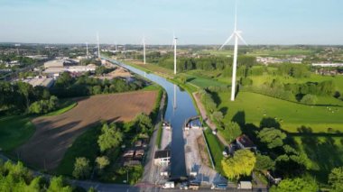 Sluis van Lot, kanaal β sel, Charleroi, Lot, Beersel, 18 Mayıs 2024, hava görüntüsü tarım arazileri ve binalarla dolu verimli kırsal bir arazide rüzgar türbinleriyle çevrili bir kanalı gösteriyor..