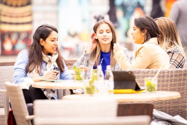 Bir grup genç kadın bir açık hava kafesinde eğleniyor, keyif ve rahatlama anlarını paylaşıyorlar.