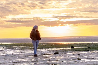 Gün batımında sakin bir plajda tek başına yürüyen bir insan huzur ve yansımayı yakalar..