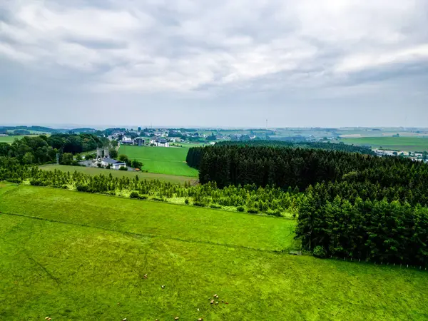 stock image Aerial photograph showcasing lush green fields, dense forests, and distant villages under a cloudy sky.