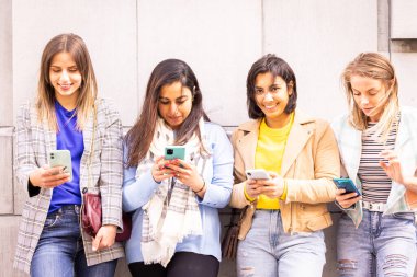 Dışarıda dikilen, gülümseyen ve akıllı telefonlarını birlikte okuyan dört kadından oluşan bir grup.
