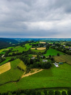 Tarım alanları, evler, tepeler ve bulutlu gökyüzü ile yeşil kırsal manzara büyüleyici tarım güzelliği sunuyor