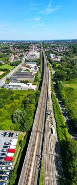 Lembeek, Halle, Vlaams Brabant, Belçika, 30 Haziran 2024, çarpıcı bir hava manzarası sergilenen tren rayları yemyeşil ve çeşitli kentsel yapılarla güzelce birbirine dolanmış.