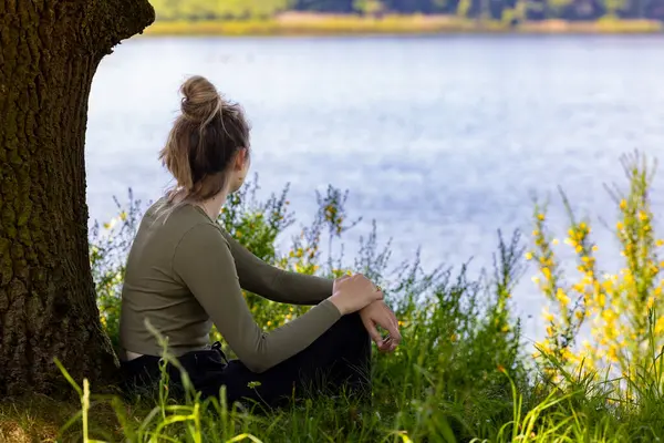 Sakin bir gölün yanındaki ağacın altında huzur ve sükunet bulan bir kadın. Doğası gereği güzellik ve sükunetle çevrili.
